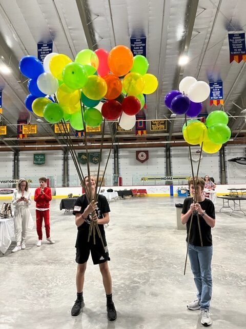 Two high school boys holding clutches of colorful helium balloons